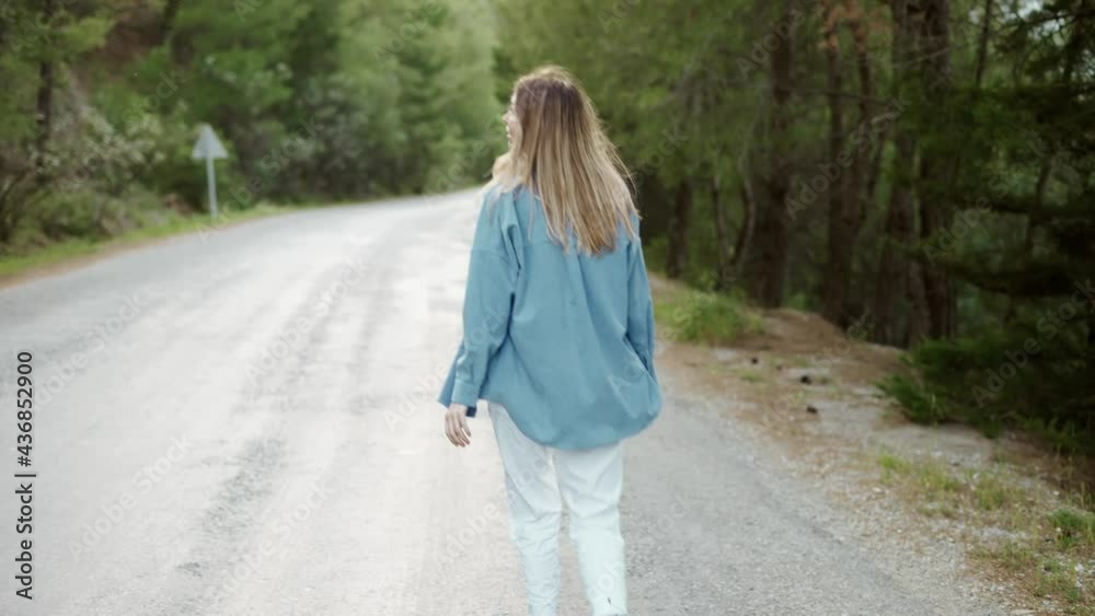 Woman walking on paving road in forest, rear view Woman walking on paving road in forest, rear view