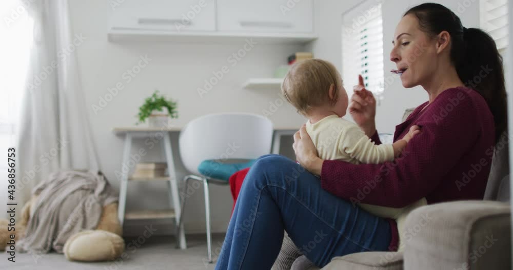Caucasian mother blowing a whistle while playing with her baby sitting on the couch at home Caucasian mother blowing a whistle while playing with her baby sitting on the couch at home