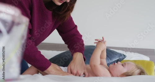 Caucasian mother changing diaper of her baby on the bed at home
