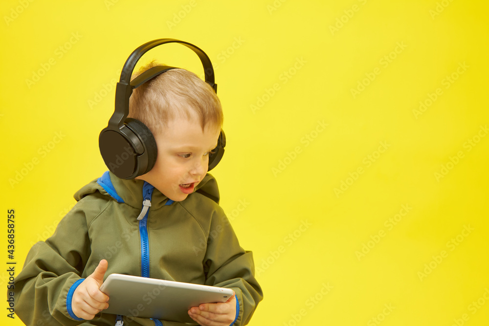 A boy wears headphones while using a tablet computer on a yellow background A boy wears headphones while using a tablet computer on a yellow background