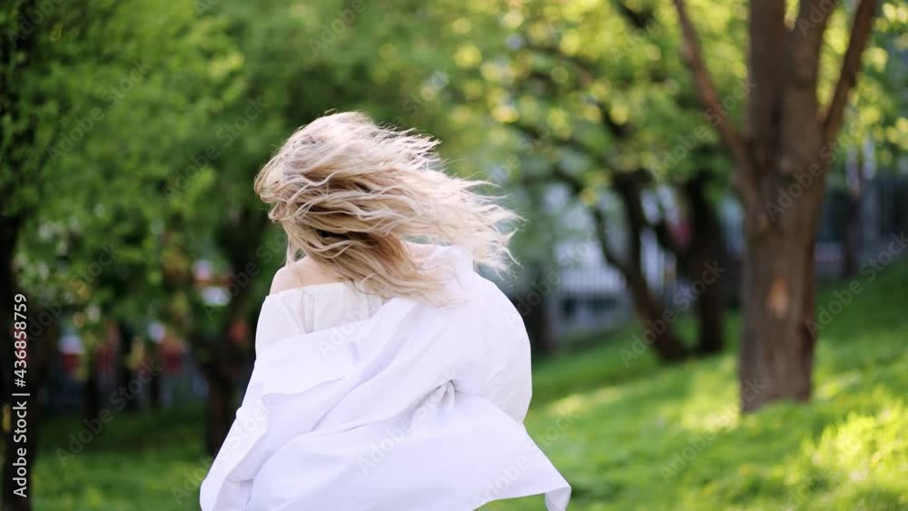 Attractive fashion model walking and spinning in park. Portrait of young beautiful blonde woman in the flowered garden in the spring time. Blossoms fall from trees. Slow motion Attractive fashion model walking and spinning in park. Portrait of young beautiful blonde woman in the flowered garden in the spring time. Blossoms fall from trees. Slow motion