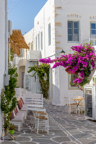 Traditional Cycladitic alley with a narrow street, whitewashed facade of a house and a blooming bougainvillea in Naousa Paros island, Greece.