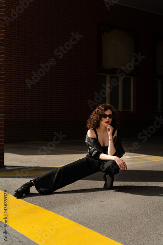 Portrait of young girl with curly hair and red lips posing on steer on building background © Dulin