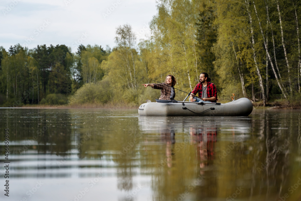 Summer vacation and activity. Young beautiful couple man and woman sailing on an inflatable boat with a fishing rod on a summer lake Summer vacation and activity. Young beautiful couple man and woman sailing on an inflatable boat with a fishing rod on a summer lake
