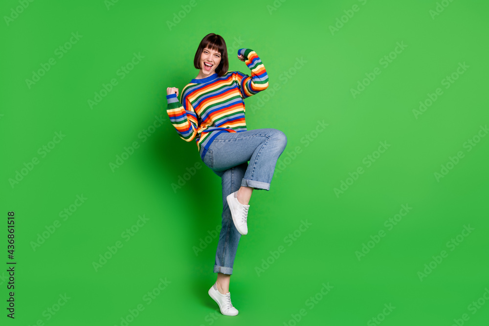 Full length photo of lucky shiny young lady dressed colorful pullover rising fists smiling isolated green color background Full length photo of lucky shiny young lady dressed colorful pullover rising fists smiling isolated green color background