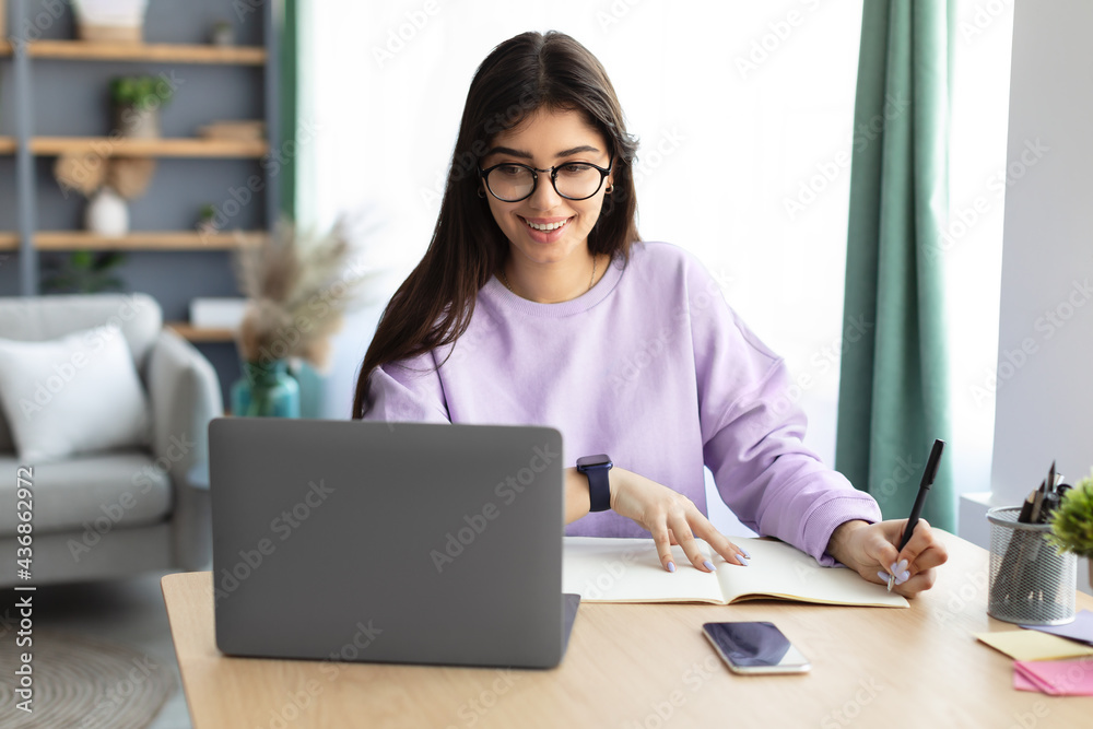 Woman sitting at desk, using computer writing in notebook Woman sitting at desk, using computer writing in notebook
