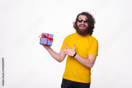 Happy young man with beard pointing at gift box over white background