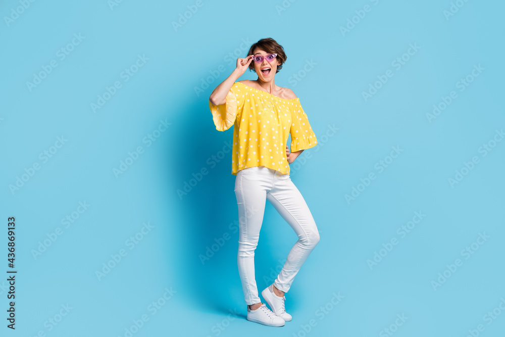 Full length photo of cool happy amazed young lady hold hand waist sunglass isolated on blue color background Full length photo of cool happy amazed young lady hold hand waist sunglass isolated on blue color background