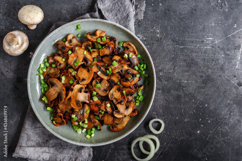 Roasted mushrooms with onion in the plate on a dark background. Top view