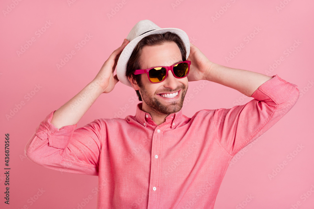 Photo of positive charming happy cool man hold hands head wear hat sunglass isolated on pink color background Photo of positive charming happy cool man hold hands head wear hat sunglass isolated on pink color background