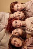 Group of young redhead female friends laying down on each other, isolated in studio on beige background. Close-up portrait of women with unusual natural red hair looking at camera confidently