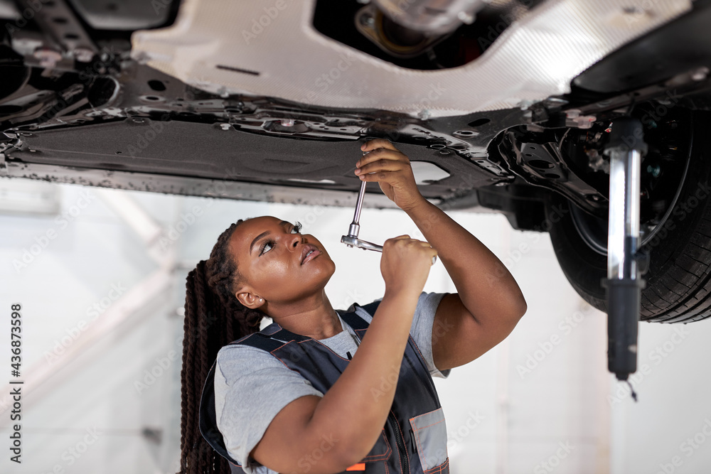 African Female auto mechanic work in garage, car service technician woman  in overalls check and repair customer car at automobile service center,  inspecting car under body and suspension system Stock Photo