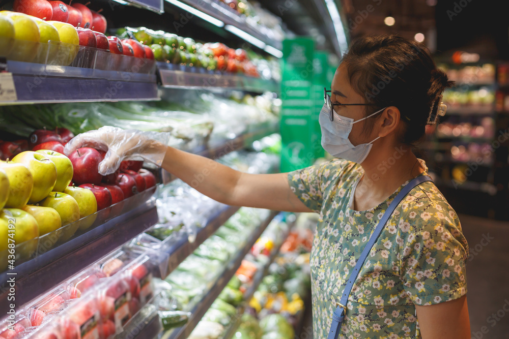 Woman wearing a surgical mask and plastic gloves handing a plastic bag with some fruits.shopping concept.
