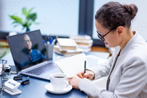 Woman is looking at laptop. Communication by video conference. Photo of computer screen with man. Business colleagues is discussing work tasks by online chat from home office. Distant job concept.