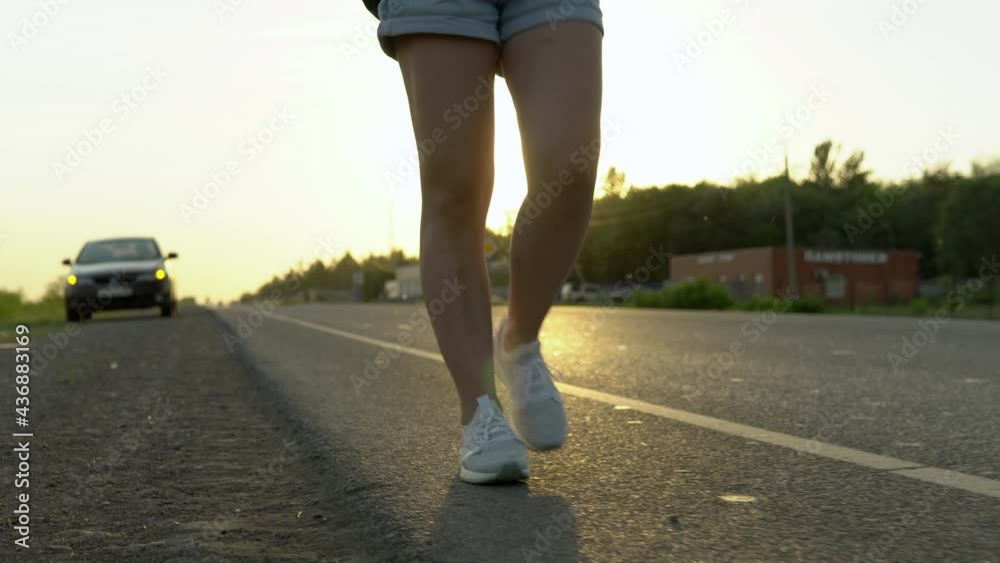 Close-up of the girl's legs against the background of a faulty car. A woman walks along the road. Close-up of the girl's legs against the background of a faulty car. A woman walks along the road.
