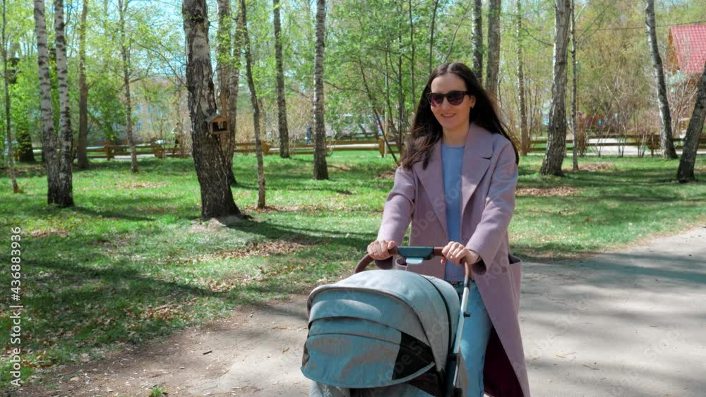 Happy mom in a coat is walking in the park with a stroller. Mothers Day. Happy mom in a coat is walking in the park with a stroller. Mothers Day.