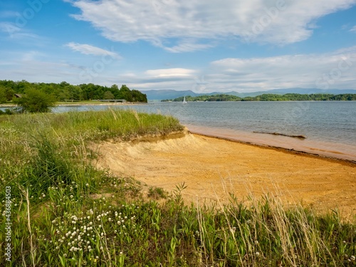 Douglas Lake in the spring in Tennessee with the Great Smoky Mountains in the background  the water and sandy shore with a blue sky filled with clouds in the distance.