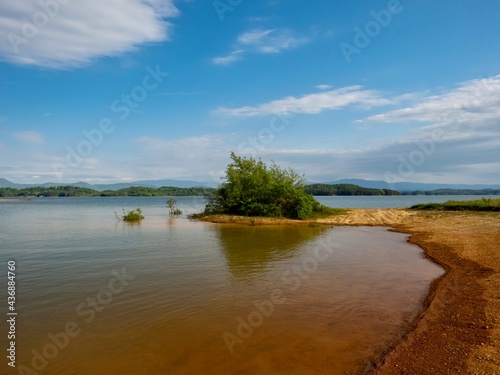 Fototapeta Naklejka Na Ścianę i Meble -  Douglas Lake in the spring in Tennessee with the Great Smoky Mountains in the background, the water and sandy shore with a blue sky filled with clouds in the distance.
