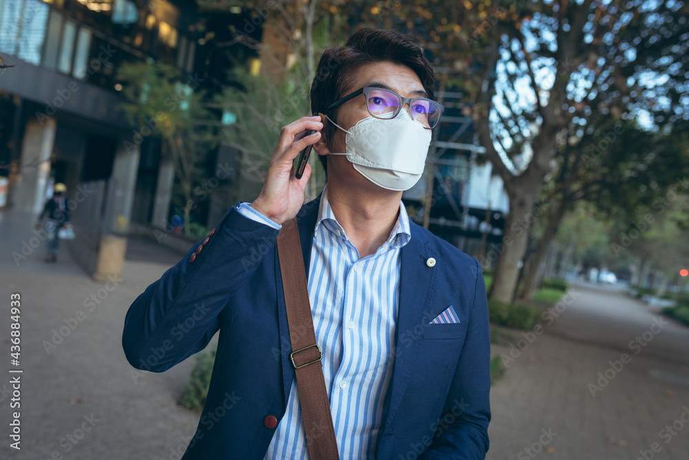 Asian businessman wearing face mask using smartphone in city street Asian businessman wearing face mask using smartphone in city street