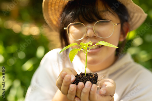Smiling asian girl wearing glasses and straw hat, holding plant in garden