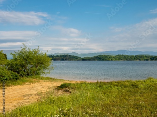 Douglas Lake in the spring in Tennessee with the Great Smoky Mountains in the background, the water and sandy shore with a blue sky filled with clouds in the distance. © Christina Saymansky