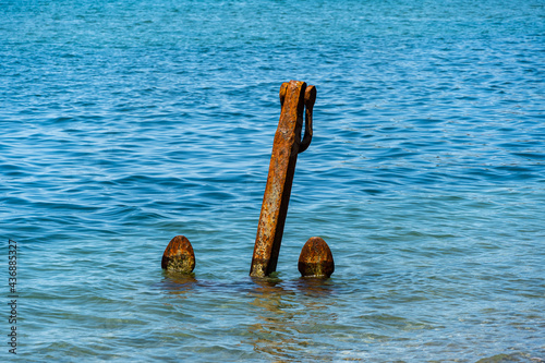 Big Anchor stands upright in shallow water near coast. Beach in Arkhipo-Osipovka. Close-up. Anchor is rusty. Sea water of emerald color. Black Sea coast of Caucasus.