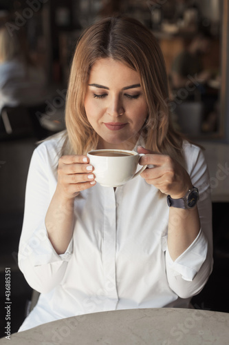 Beautiful business woman 30-40 years old smelling the aroma of coffee in a cafe