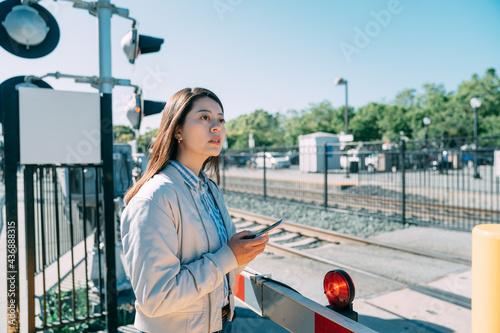 lost asian female traveler waiting at a railroad crossing is looking into distance while using gps on the phone for directions on a sunny day in California  usa