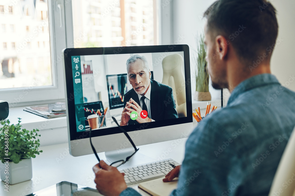 Confident young man talking to collegue by video call while sitting in office Confident young man talking to collegue by video call while sitting in office