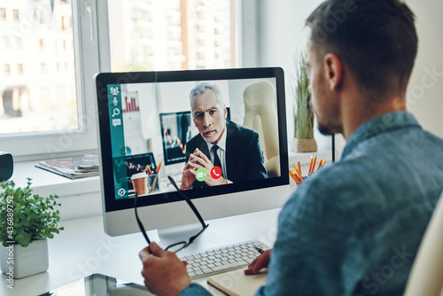 Confident young man talking to collegue by video call while sitting in office