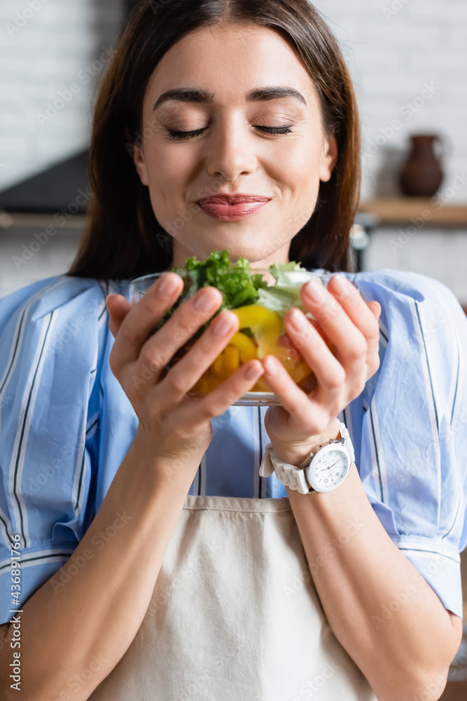 smiling young adult woman enjoying smell of fresh vegetables salad with closed eyes in kitchen smiling young adult woman enjoying smell of fresh vegetables salad with closed eyes in kitchen