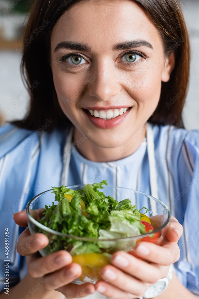 portrait of smiling young adult woman holding fresh vegetables salad in hands on blurred background portrait of smiling young adult woman holding fresh vegetables salad in hands on blurred background