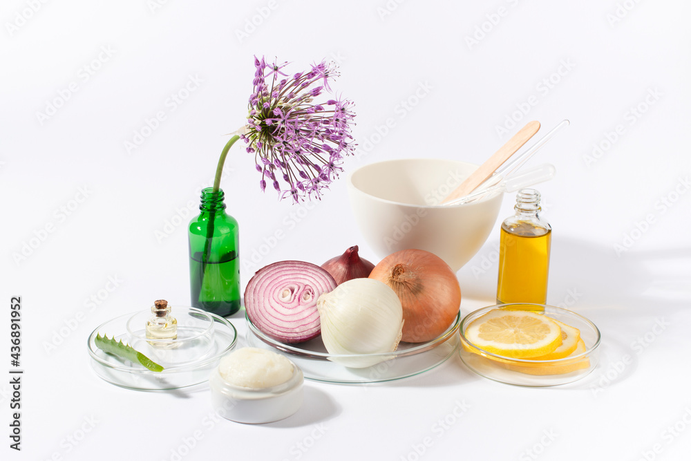 Onions, laboratory glassware with oil, cream, lemon, Aloe vera, and Allium giganteum flower on white background.