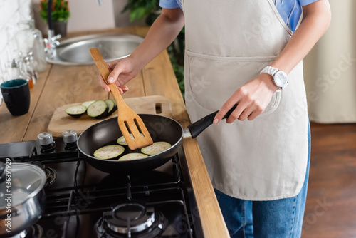 Φωτογραφία cropped view of young adult woman frying slices of eggplant in pan and using spa