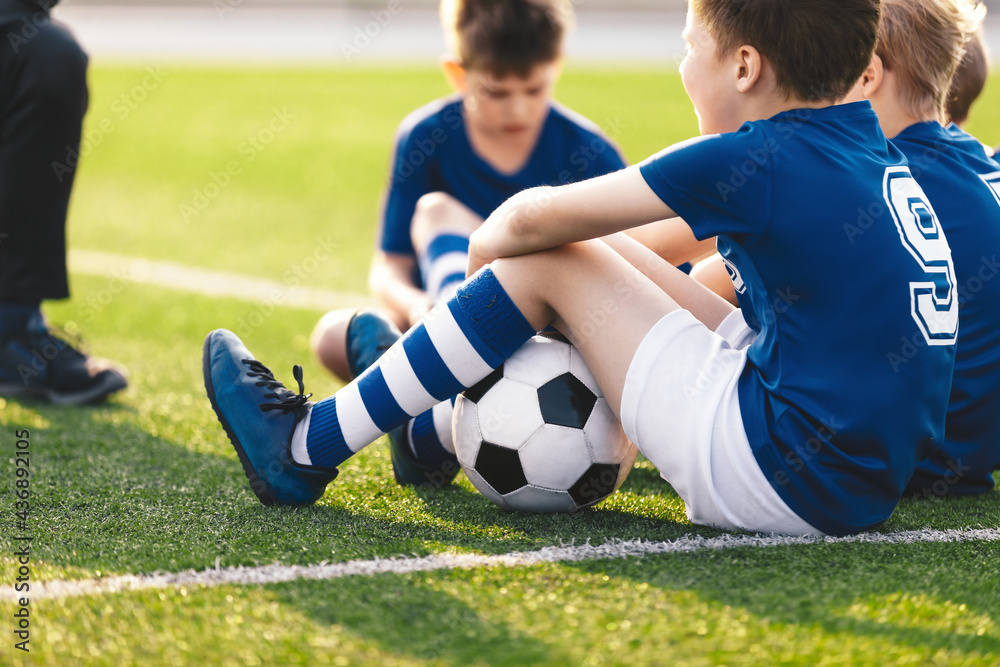 Kids Sitting on Grass Soccer Pitch. Boys in Blue Football Jersey Shirts. Happy Kids on Football Training Camp. Children Playing Sports