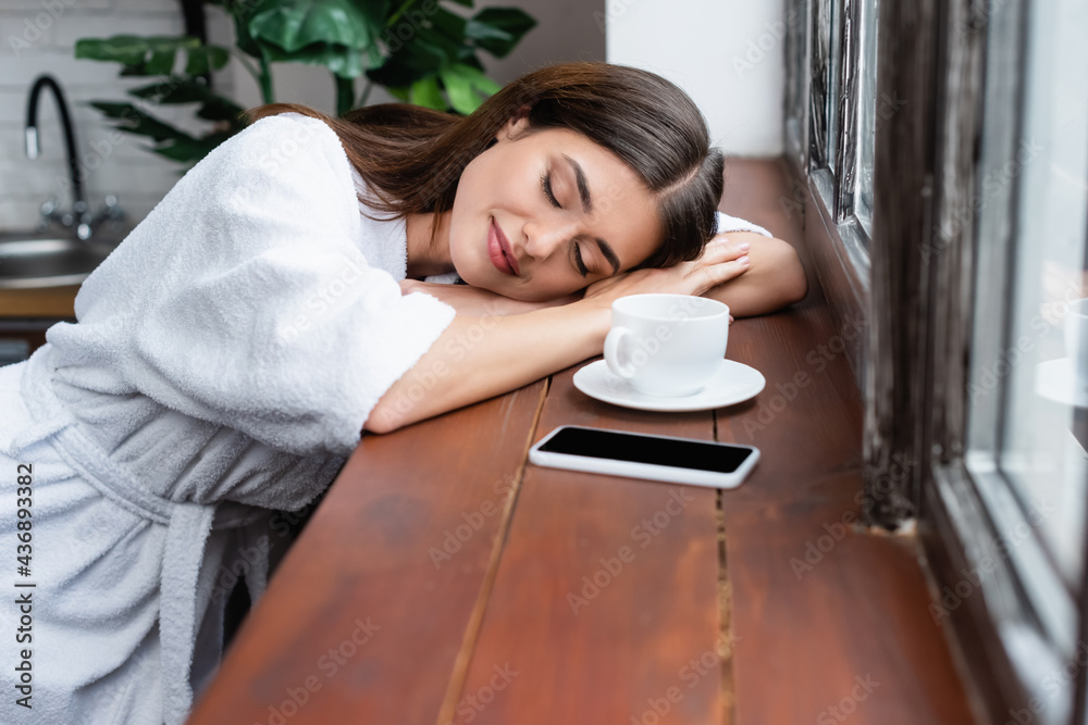 young adult woman sleeping near cellphone and cup of coffee at sill in living room