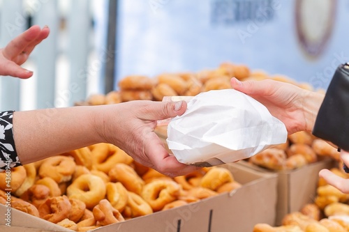 Woman's hands selling doughnuts rolled in paper for sale with doughnuts in bulk, food concept. photo