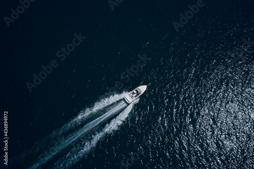 Drone view of a boat sailing. Top view of a white boat sailing to the blue sea. Travel - image. Large white boat fast movement on blue water aerial view. Motor boat in the sea.
