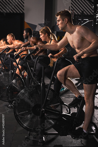 strong men and women riding an exercise bike, people exercising on stationary bike together, concentrated on cardio training