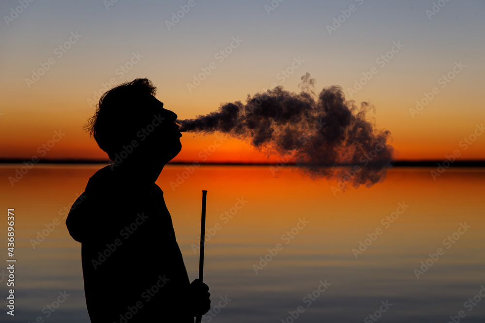 Fototapeta premium Exhales smoke at sunset. Smoking hookah.