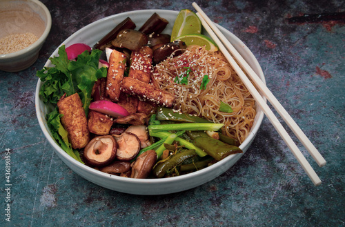 Vegan tofu, mushroom, pepper, eggplant and rice nooodles bowl in white bowl dish with chopsticks