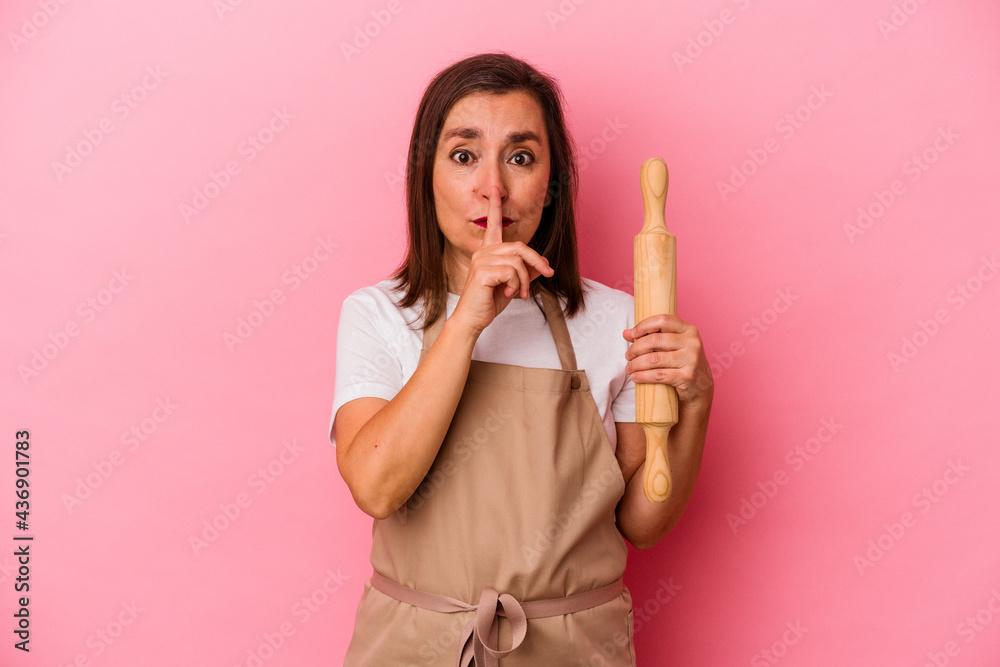 Fototapeta premium Middle age pastry chef woman isolated on pink background keeping a secret or asking for silence.