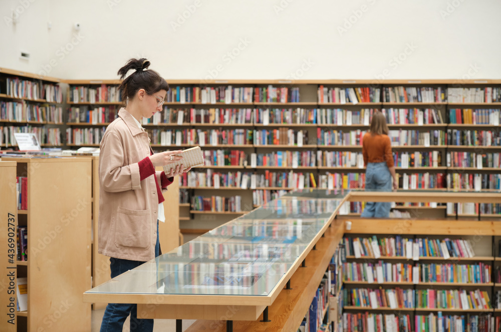 Young people studying in the library and choosing books for reading Young people studying in the library and choosing books for reading