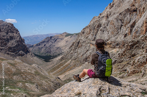 A woman with a backpack sits on the pass of the high mountains of Aladaglar and looks into the valley. Turkey