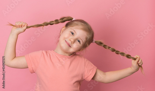 Portrait of little playful girl with pigtails smiling on pink background.