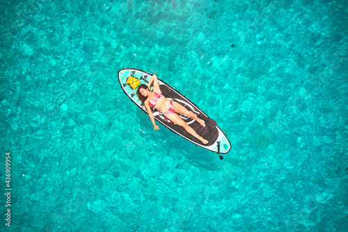 Aerial shot of woman laying on paddle board with a crystal clear turquoise water background © Daniel