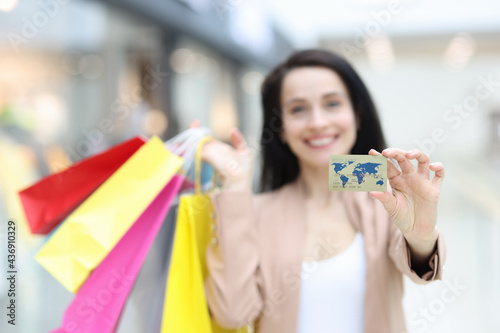 Smiling woman holding purchases and plastic bank card in shopping mall