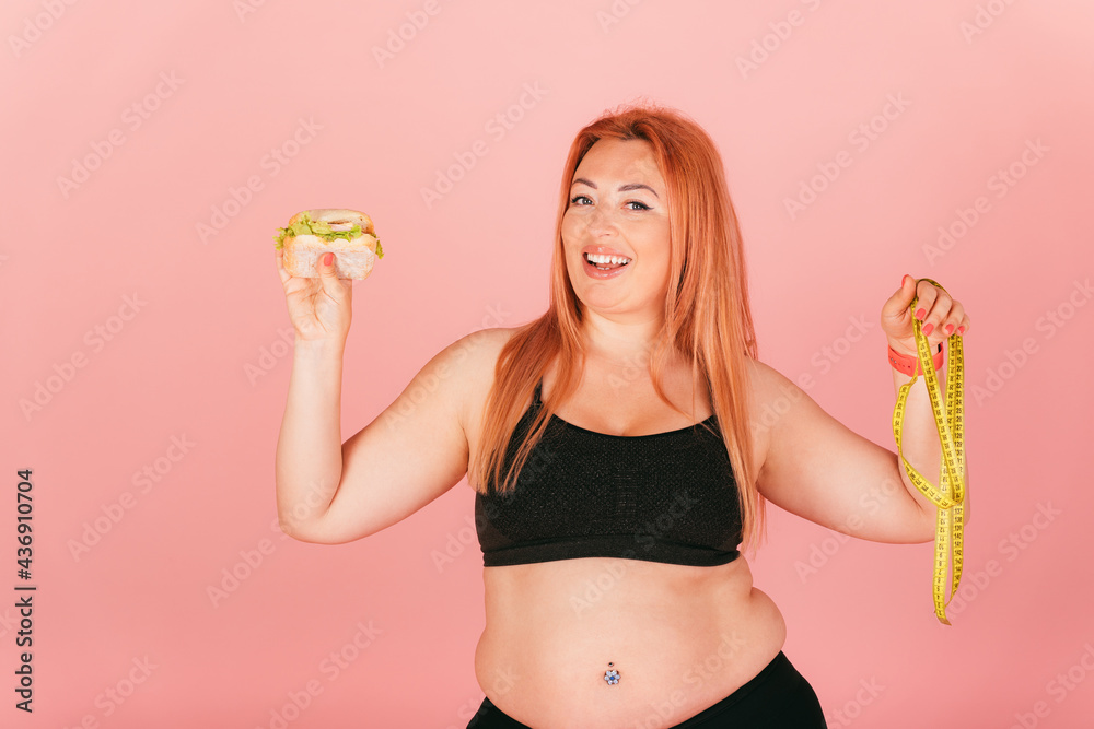 Happy plus size woman wearing sporty outfit holding fast food burger Happy plus size woman wearing sporty outfit holding fast food burger