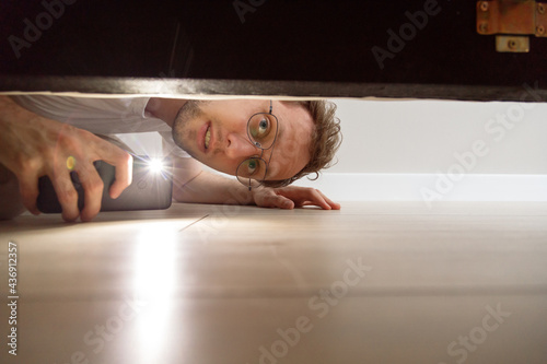 Quadro su tela Man with flashlight looking under the bed