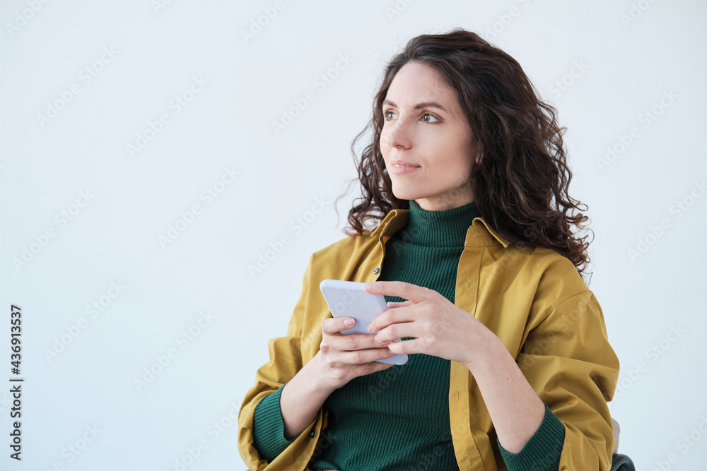 Young pretty woman with curly hair sitting on chair with mobile phone isolated on white background Young pretty woman with curly hair sitting on chair with mobile phone isolated on white background